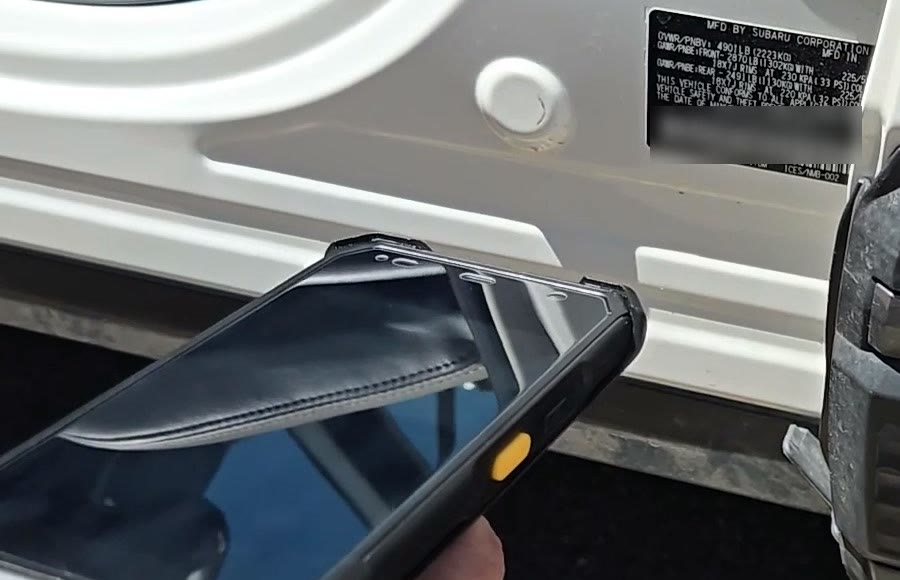A handheld scanner from the startup kit reading the VIN barcode on a vehicle door jamb